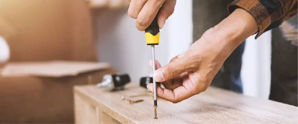 Nahaufnahme einer Hand, die mit Schraubendreher eine Schraube in ein Holzregal dreht. Symbolbild für Möbelmontage, Aufbauservice und fachgerechte Möbelinstallation im Wohnbereich.